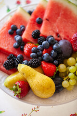 Top view on a plate with sliced fruits and berries on a beautiful white plate with fruit smoothie on the table. Watermelon, strawberry, blueberries, blackberry and grapes. Healthy snack.