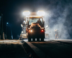 Industrial pavement truck is laying fresh asphalt on construction site at night. Road service repairs the highway	
