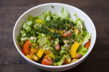 Closeup of chopped organic garden vegetables in a white bowl: tomatoes, cucumbers, yellow pepper, lettuce leaves and dill. Healthy nutrition. Cook at home.