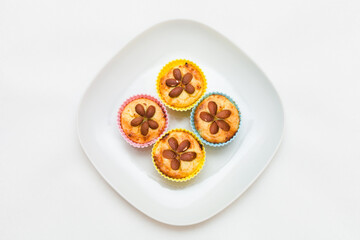 Close-up of homemade vanilla cakes with whole almonds in multicolored silicone cups on a white plate. Healthy snack.