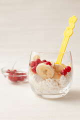 Cottage cheese with banana slices and red currant berries in a glass cup. Delicious and healthy breakfast, located in a glass cup on a light background