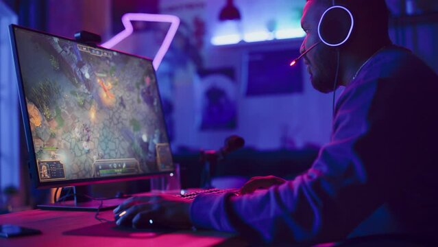 Excited Gamer Playing PRG Strategy Video Game in Which Players Fight in a Battle Royale Tournament on His Personal Computer. Room and PC with Neon Lights. Stylish Black Man in Cozy Room at Home.