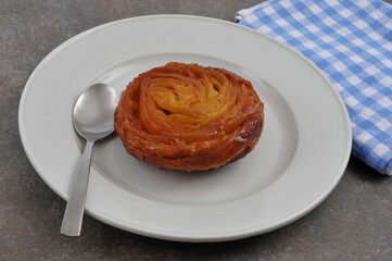 Kouign-amann dans une assiette avec une cuillère en gros plan sur fond gris