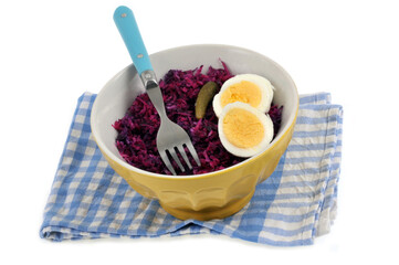 Repas diététique dans un bol de chou rouge avec des oeufs durs et une fourchette posé sur une serviette à carreaux sur fond blanc