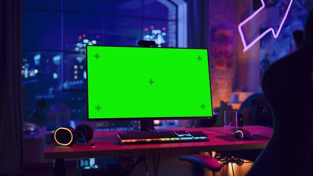 Gaming at Home: Empty Gaming Station with Player's Personal Computer with Green Screen Chroma Key Display Standing on a Wooden Desk in Stylish Loft Apartment with Neon Lights. Zoom In Shot.