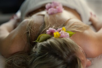 schöne Frau geschmückt mit Blüten liegend auf Massagebank