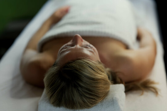 sch&ouml;ne blonde Frau liegend in weisses Handtuch gewickelt auf Massageliege, Massage zuhause, spa 