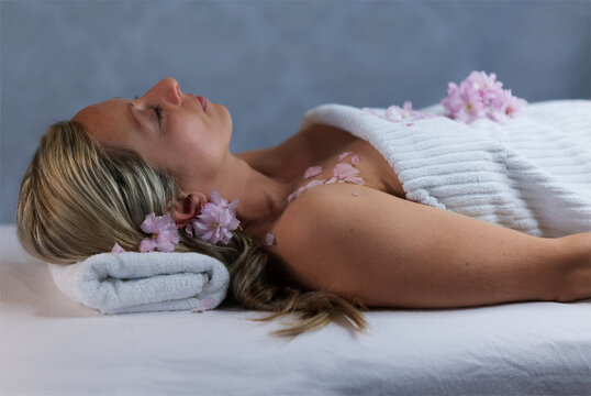 sch&ouml;ne blonde Frau liegend auf einer Massage Liege, bedeckt mit einem weissen Handtuch und rosa Kirschbl&uuml;ten geschm&uuml;ckt