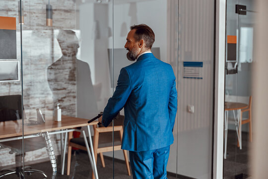 Back view of man in a stylish suit entering the office while opening glass doors