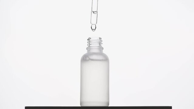 Hand dripping cosmetic product from pipette into transparent bottle. Glass container for serum, lotion or toner for skin care
