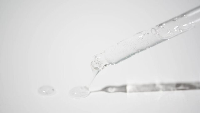 Drops of cosmetic product dripping on white background, table. Pipette with liquid transparent serum for face and skin