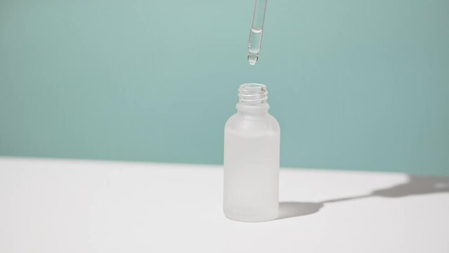 Cosmetic product in glass bottle drips from glass pipette. Drops of lotion or serum for skin care. Cosmetics concept on white and blue background