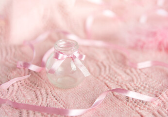 Fototapeta na wymiar small bottle with a pink ribbon on a delicate pink background