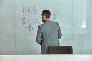 Back view of adult man putting his ideas on white board during a presentation in the office