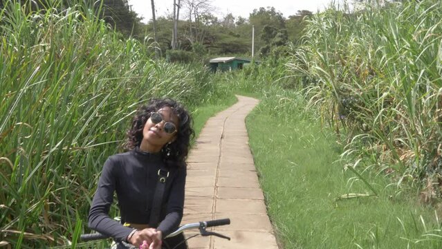 aerial shot of a beautiful black woman on a bike standing on a little paved road between high african grass in karuna forest