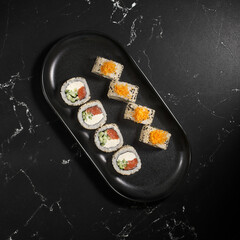 Sushi rolls in sesame with avocado and cream cheese on a black background