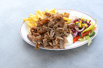 Thin slices of doner kebab meat with french fries, salad and yogurt dip sauce on a plate and a gray table, copy space, selected focus - 502172803