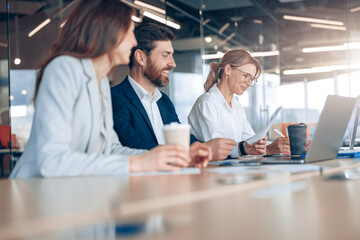 Team of young happy businessmen communicating together during meeting and drink coffee in office . 