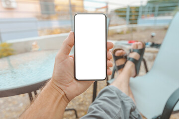 Man sitting on apartment terrace with feet on the table looking at mobile smart phone mockup screen