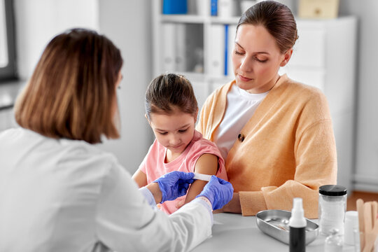 medicine, healthcare and pediatry concept - female doctor or pediatrician attaching medicinal patch to arm of little girl patient with mother at clinic