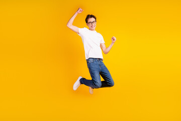 Full size photo of young cheerful guy jump ump rejoice victory success fists hands isolated over yellow color background