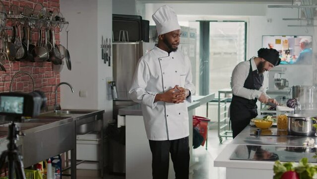 African american cook filming cooking show vlog on camera, making delicious meal with culinary recipe. Male chef in uniform recording online gastronomy class with professional food dish.