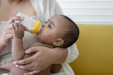 African newborn baby sucking milk from bottle and holding mother finger while lying in young mother...
