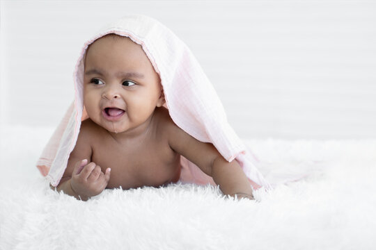 Portrait of Little African newborn baby girl smiling crawling on bed with towel on head to clean after bath. Innocent infant expression. White background