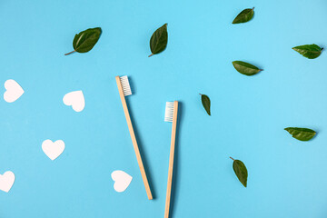 Two wooden bamboo eco friendly toothbrushes, green leaf, white heart on blue color background in studio. Dental care, eco friendly, reuse and valentines day concept. Flat lay, top view, copy space