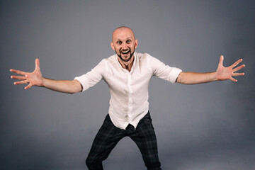 A bald guy in a white shirt and dark plaid pants throws up his hands on a gray background.