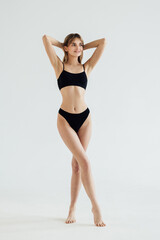 Fototapeta na wymiar Sporty woman in black bikini posing on grey background. Beauty and body care concept