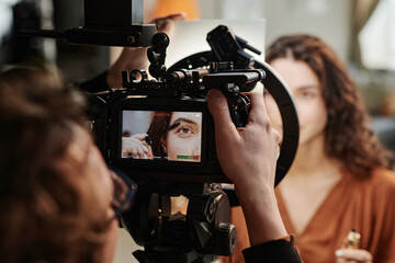 Screen of video camera with part of face of fashion model applying new volume mascara on eyelashes...