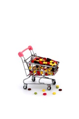A miniature shopping cart with a bunch of pills in different colors.