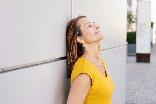 bestager woman leans against a wall with closed eyes and relaxes