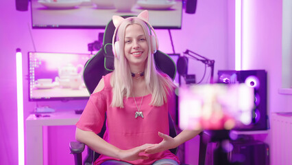 Cute blonde gamer girl in pink cyberspace room recording video with smartphone
