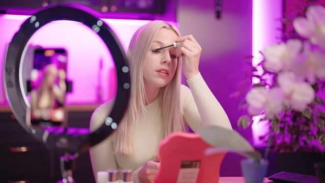 Cute female Influencer at home in pink kitchen record eyelashes brushing tutorial