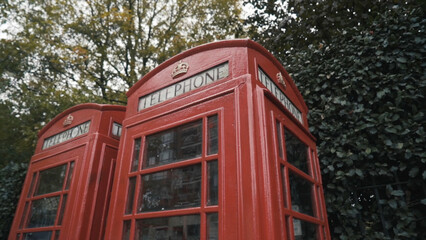 Close-up of the traditional red telephone boxes in London against green trees on the street. Action. National symbols of England