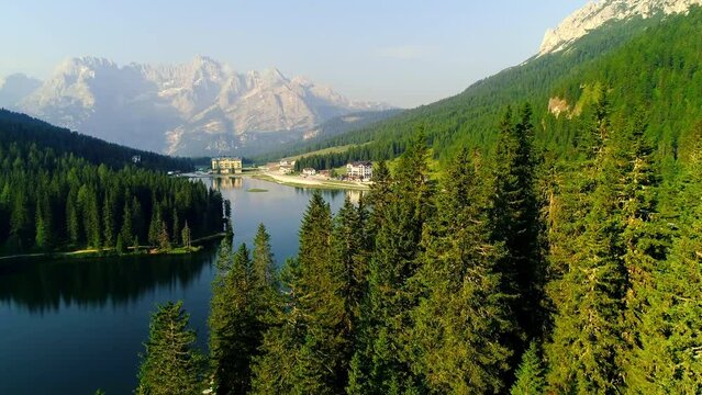 Aerial flight adove stunning lake in Alps. High mountain peaks sharp cliffs sunrise Dolomites