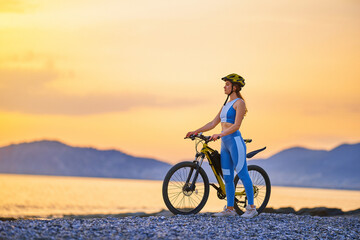 Active young fitness woman wearing sportswear and helmet standing alone with bike outdoor