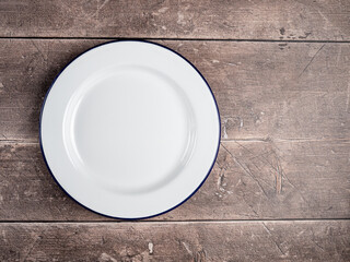 isolated traditional White Enamel plate with navy blue rim used for baking and cooking on a rustic wooden table background