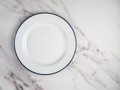 isolated traditional White Enamel plate with navy blue rim used for baking and cooking on a rustic white marble background