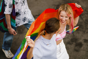 Young lesbian couple walking with rainbow flag during pride parade
