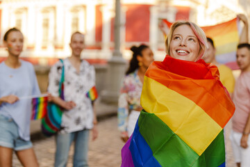 Young lesbian woman wrapped in rainbow flag smiling during pride parade