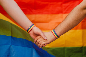 White gay couple holding hands with rainbow colorful flag background
