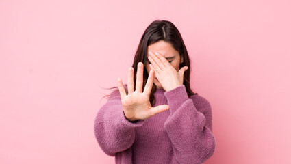 young pretty woman covering face with hand and putting other hand up front to stop camera, refusing...