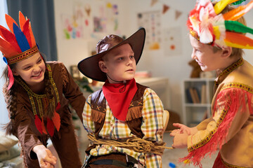 Happy children in stage costumes binding captured cowboy with rope while playing and having fun...