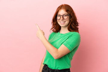 Teenager redhead girl over isolated pink background surprised and pointing side