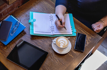 Senior woman write in notebook while sitting by the window in a small cafe. Business meeting.