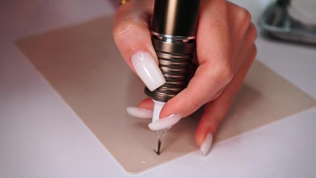 hands of a young caucasian girl with a machine for permanent makeup make a trial sketch of eyebrows on a silicone mat
