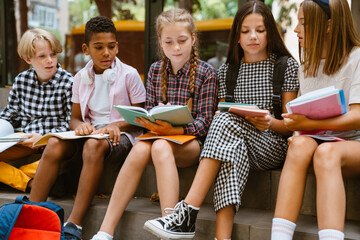 Multiracial pupils doing homework while sitting together by school